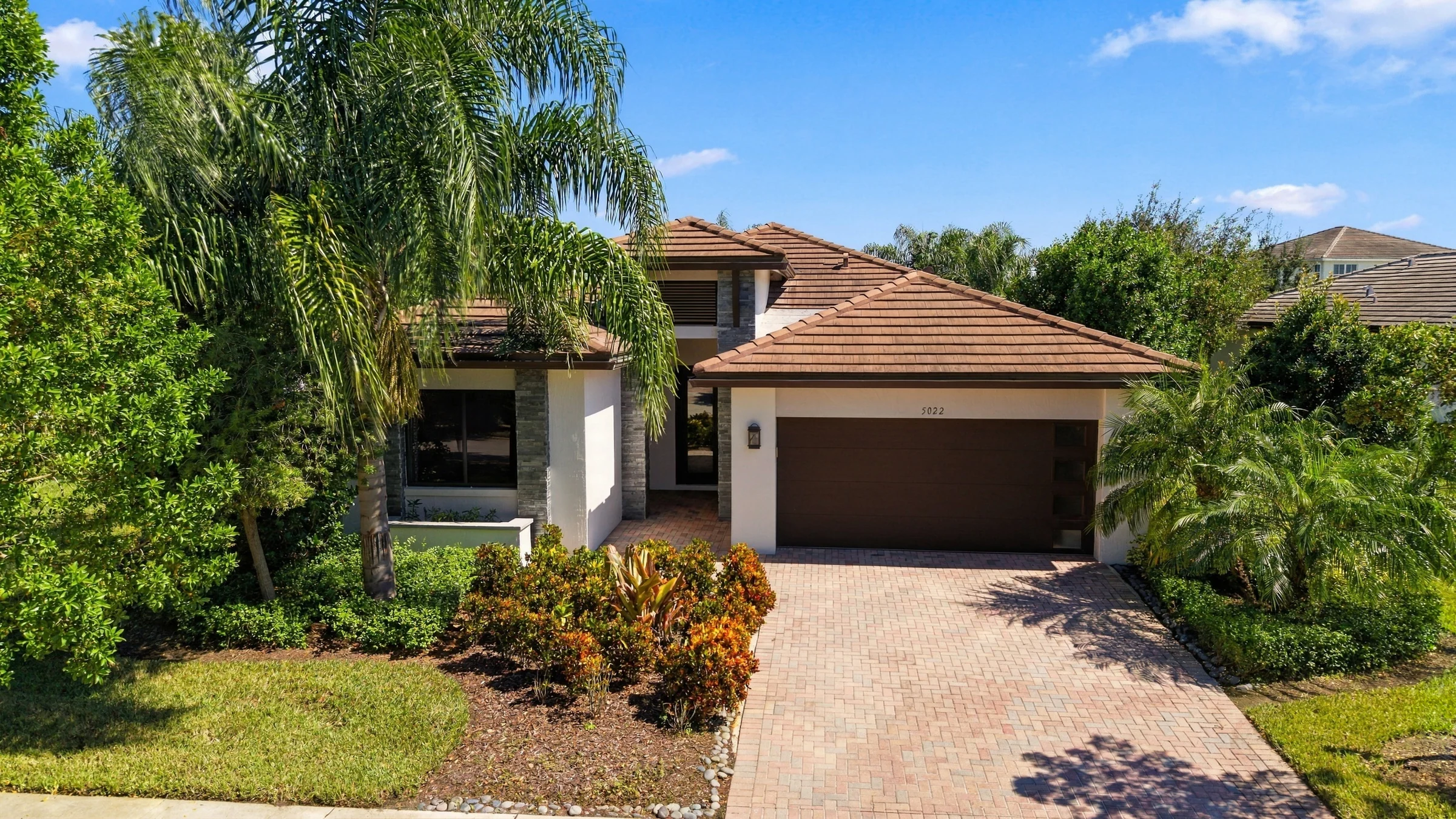 Single-story Fairmont model home with a tiled roof, paver driveway and palms in daylight