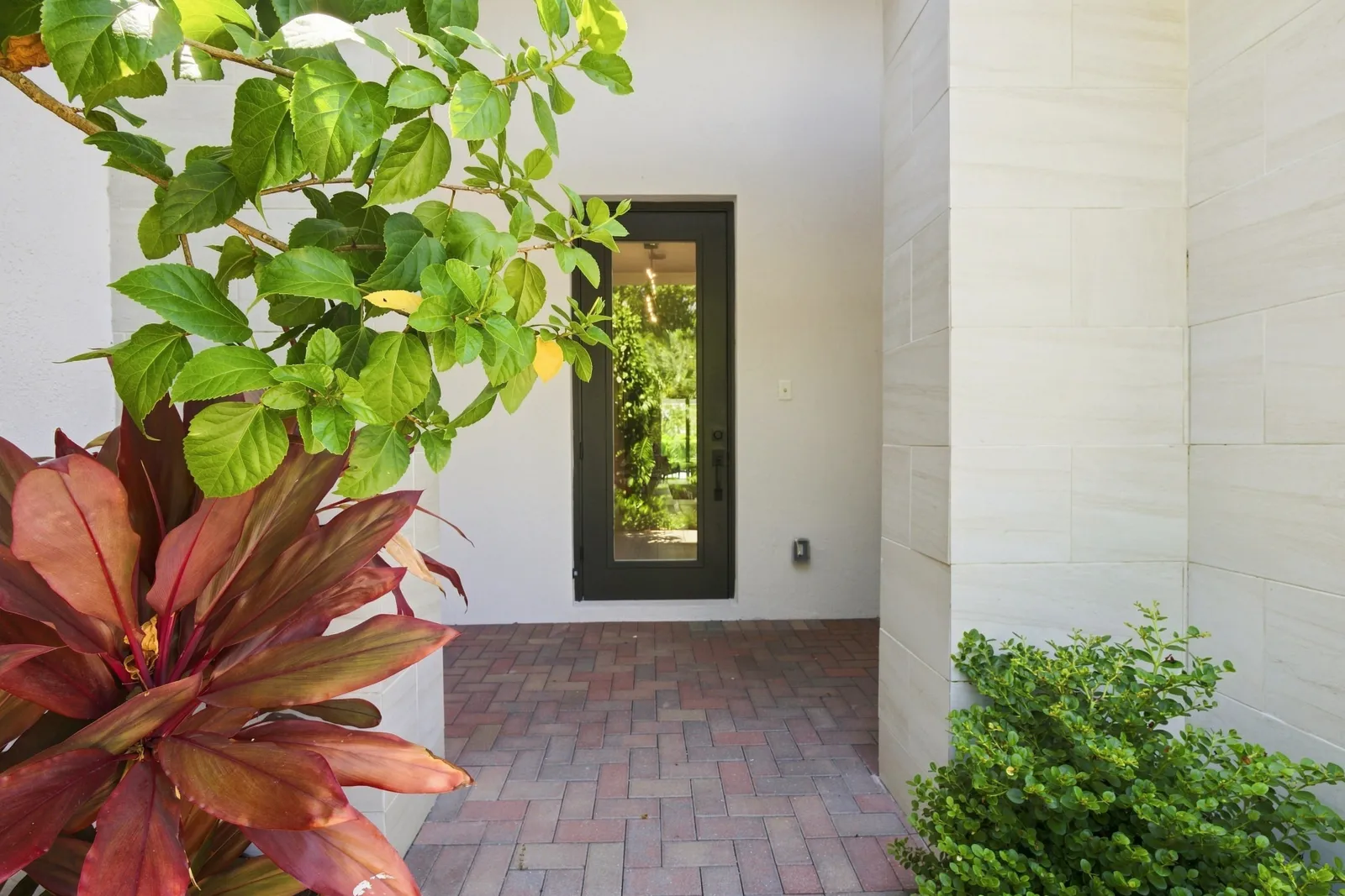 Brick courtyard entry framed by tropical plants and stone wall cladding