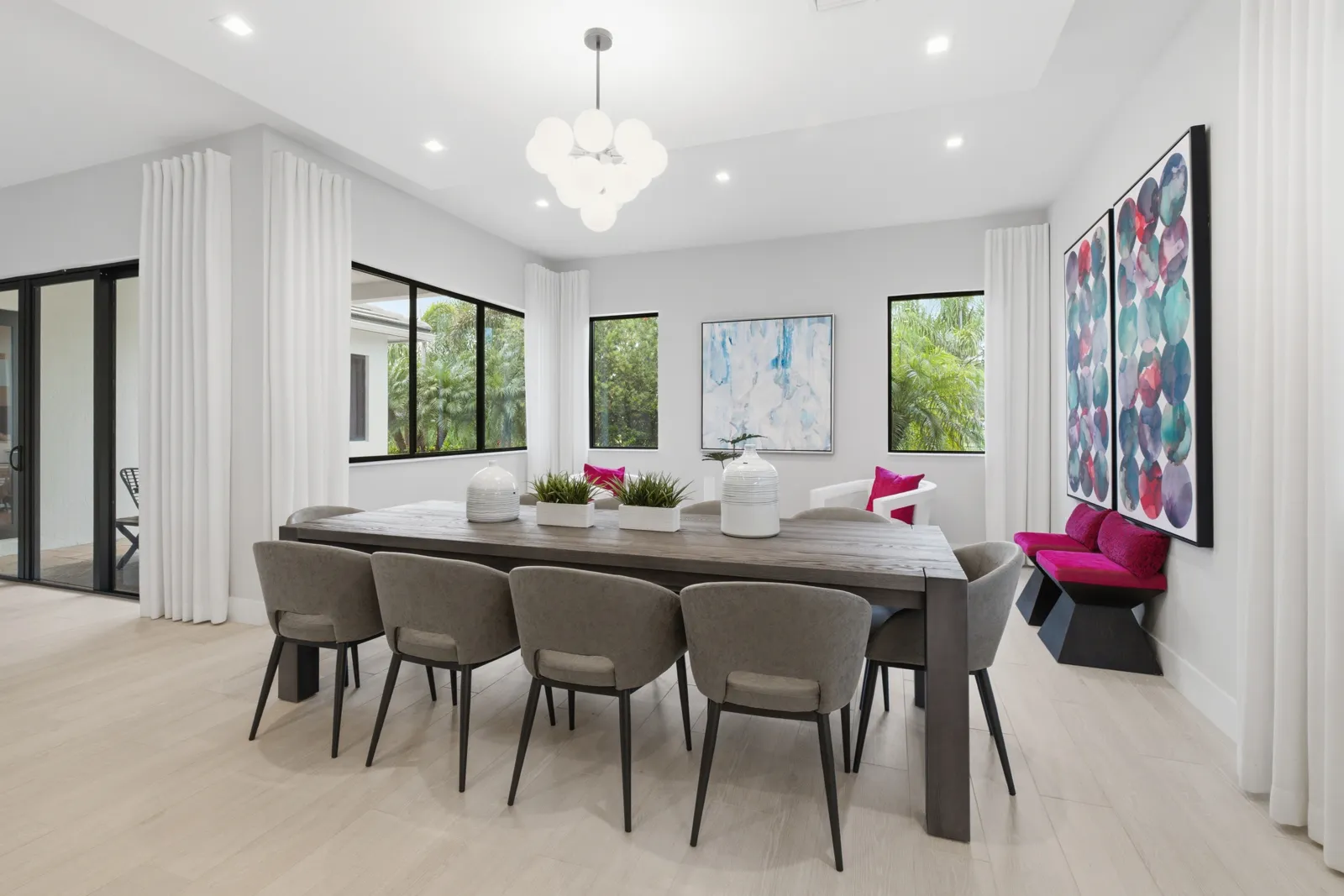 Dining area with a modern chandelier, upholstered chairs and colorful artwork