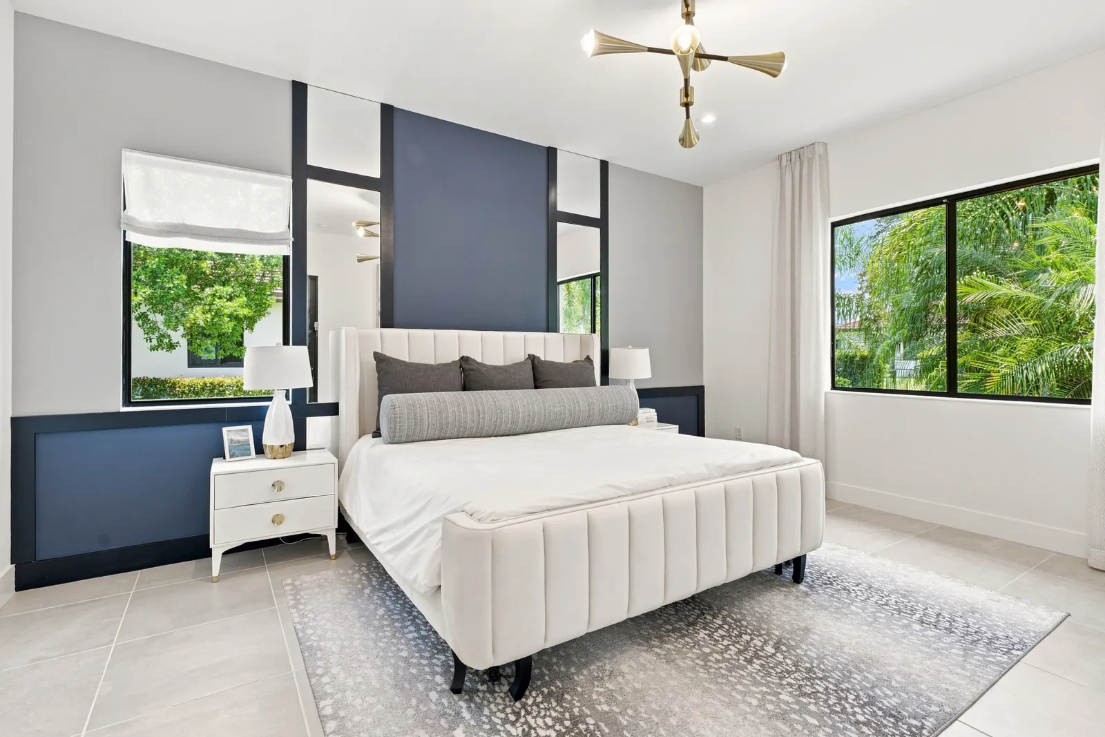 Primary bedroom with an upholstered bed, navy accent wall and gold chandelier