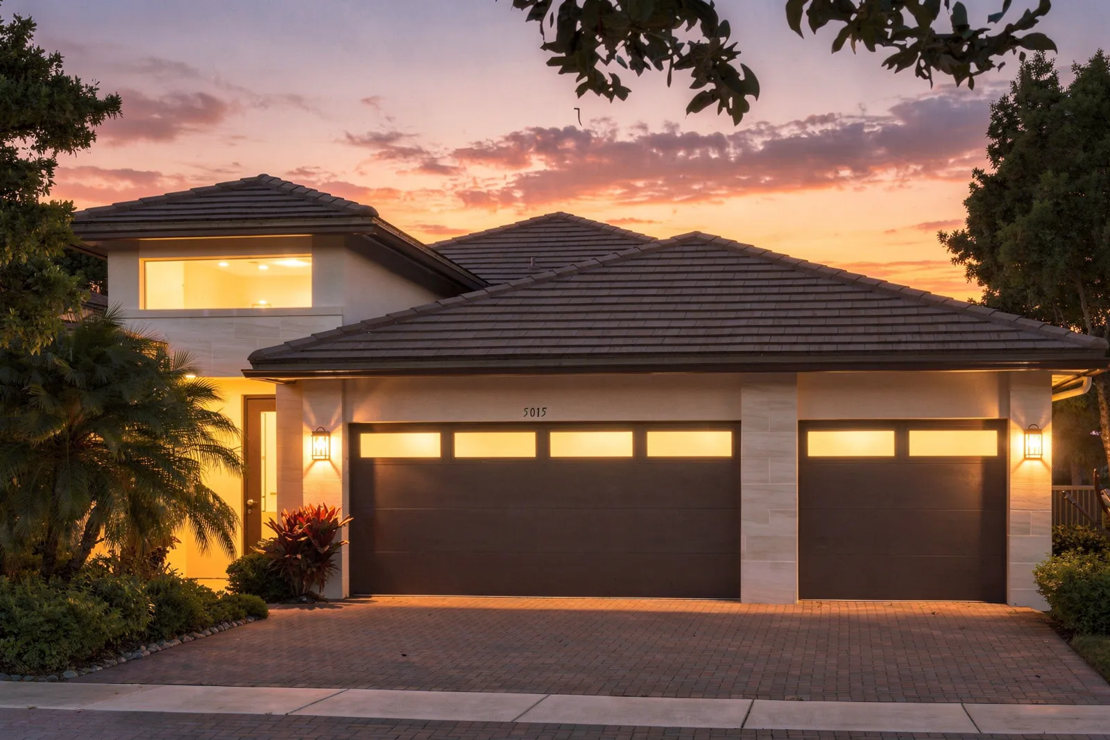Two-story home at sunset with illuminated garage windows (virtual twilight, digitally enhanced)