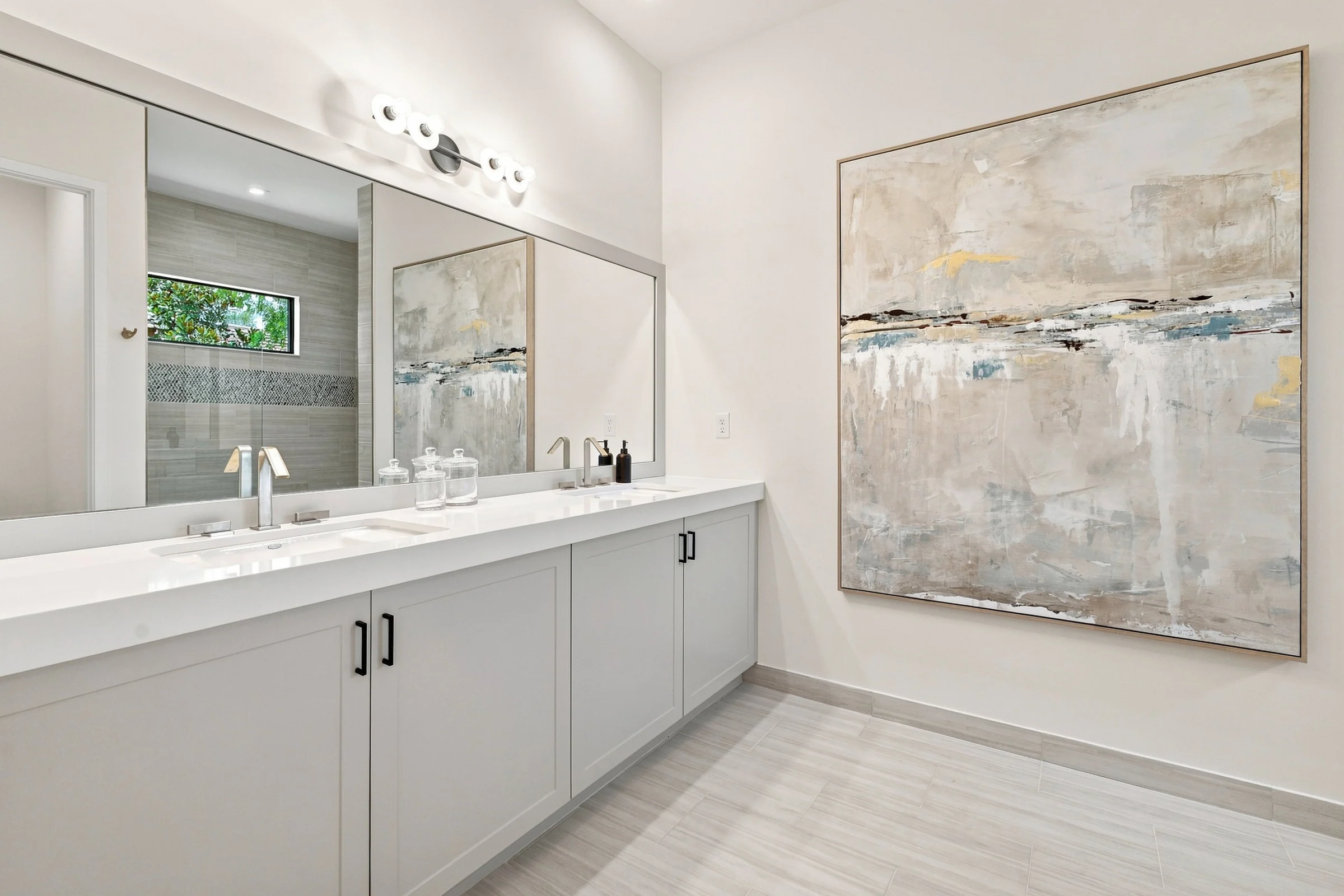 Primary bath with a long white vanity and large abstract artwork