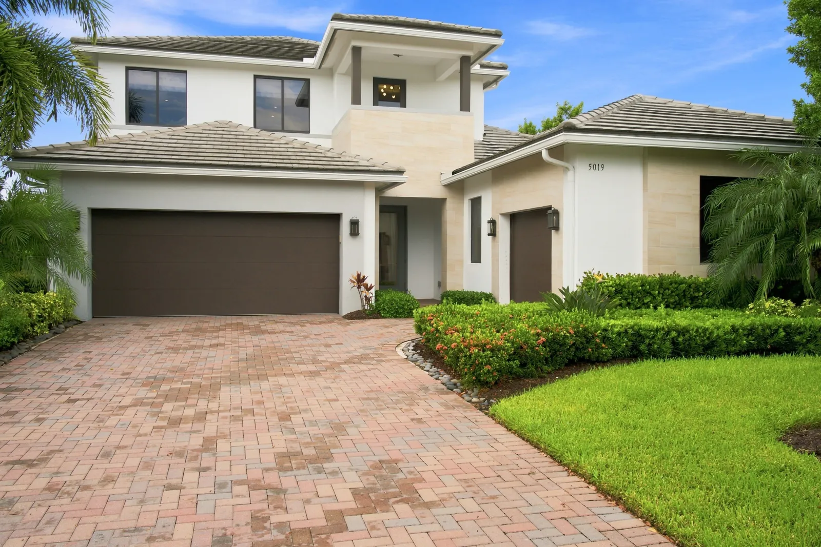 Two-story white stucco home with a paver driveway and manicured hedges