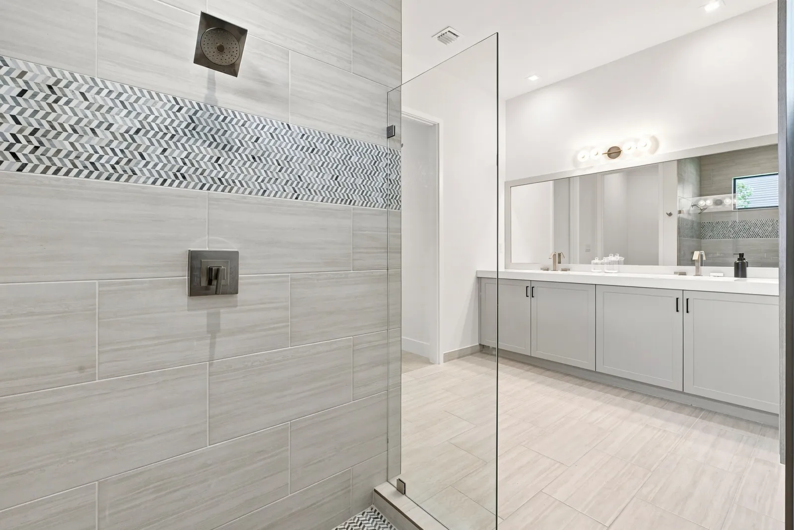 Walk-in glass shower with herringbone tile accent and rainfall head