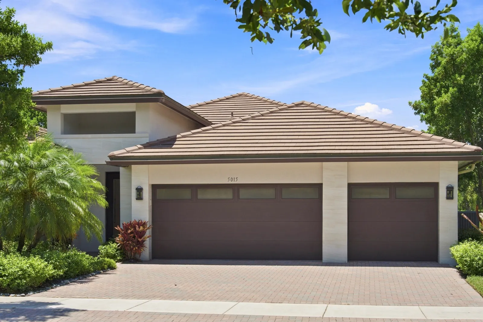 Two-story home with a tiled roof and three-car garage framed by tropical landscaping