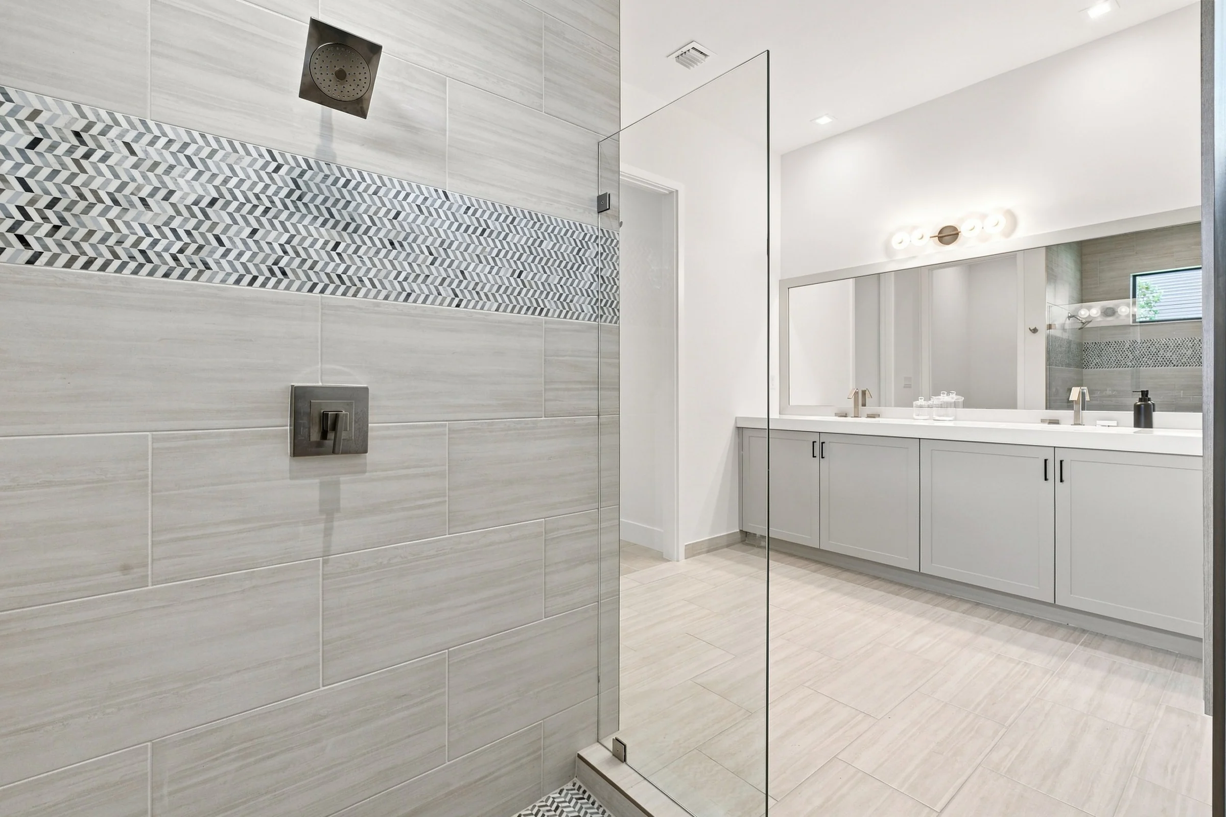 Walk-in glass shower with a herringbone tile accent