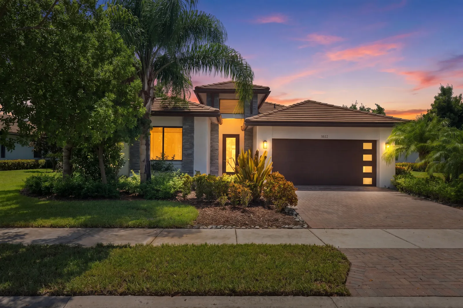 Single-story home at dusk with glowing windows and a pink and blue sky (virtual twilight, digitally enhanced)